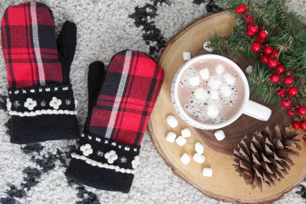 Finished flannel mittens made from an old shirt next to hot chocolate with marsmallows, greenery, pine cones, and red berries.