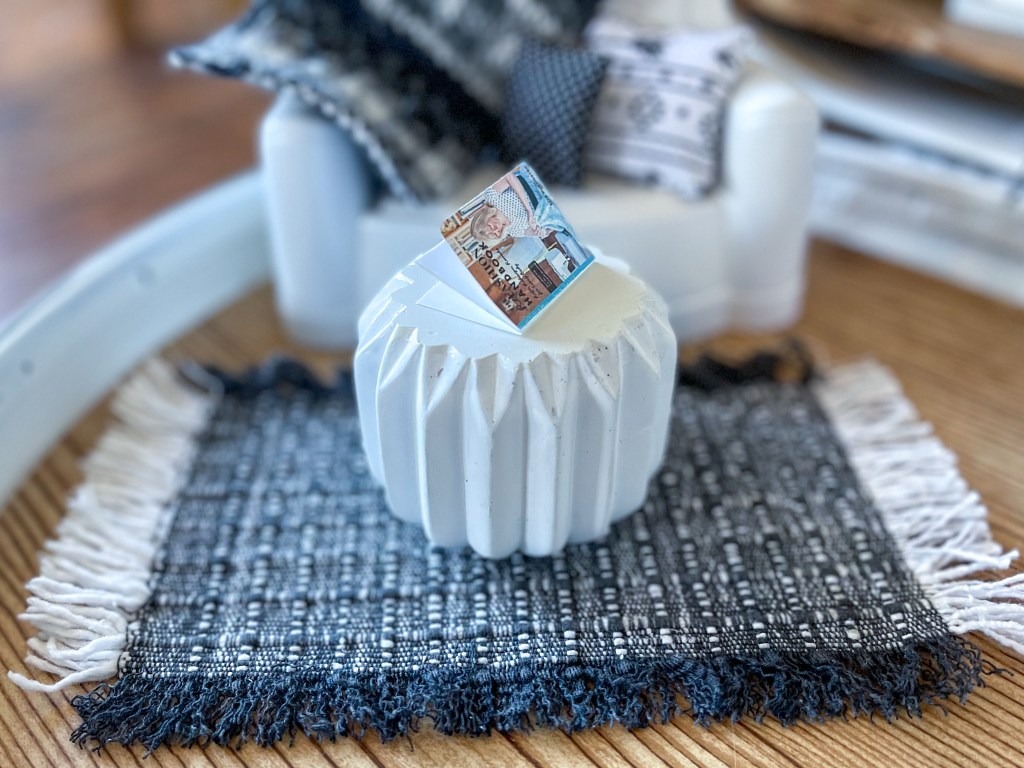 Close-up of tiny white coffee table, book and rug in a dollhouse made in a vintage suitcase.